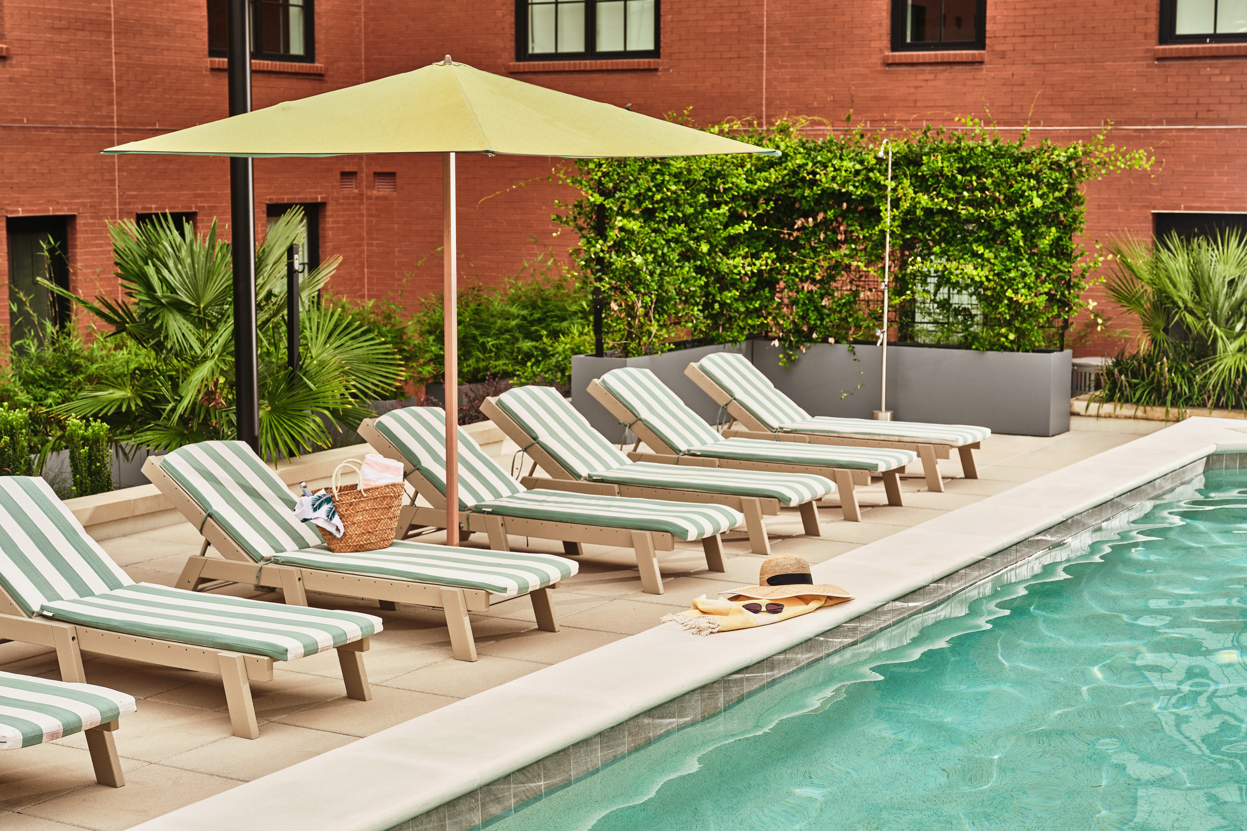 Outdoor swimming pool and striped lounge chairs within The Ann Savannah's brick courtyard.