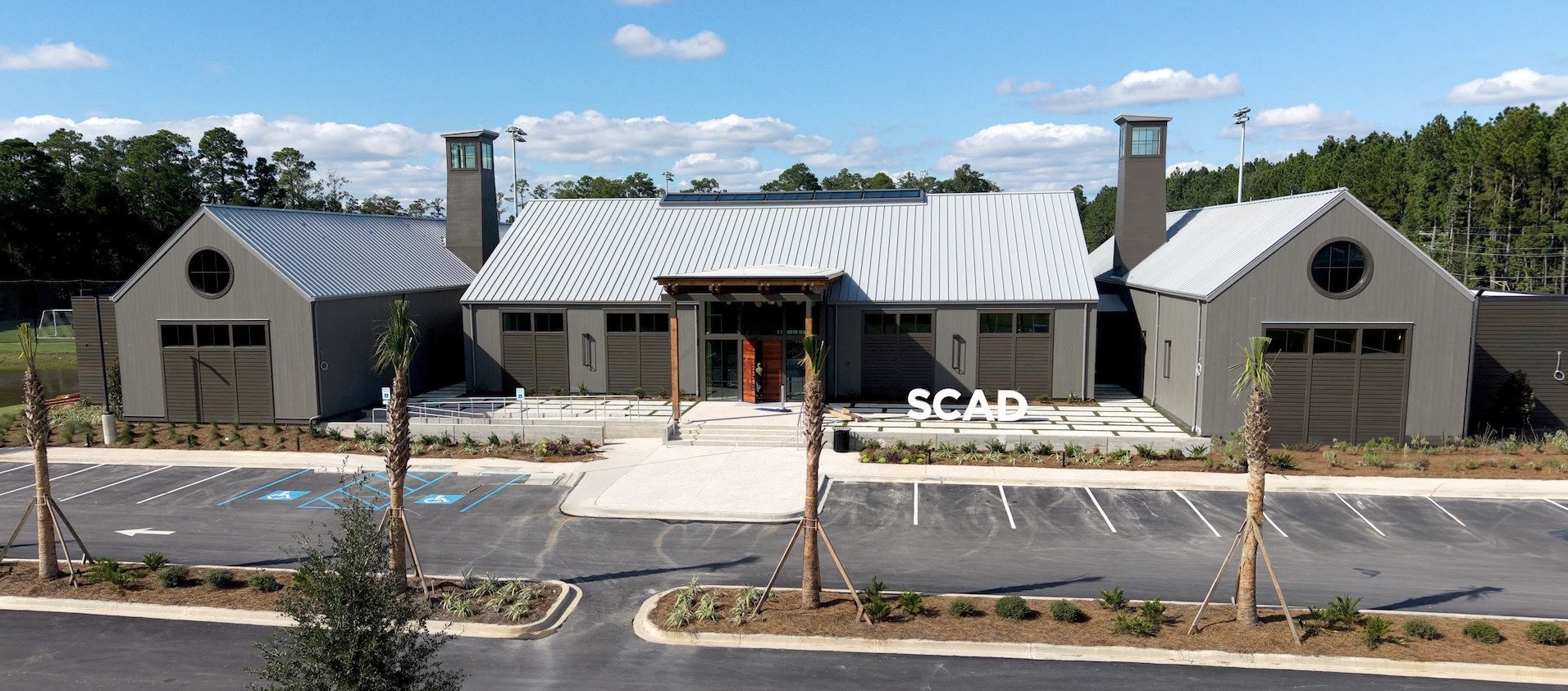 The completed SCAD field house exterior, with a central entrance, gabled wings and SCAD sign beside the front steps.